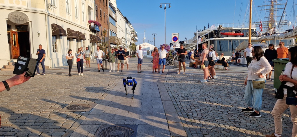 Robothunden Spot lufter seg på brygga i Arendal for mange mennesker som ser på.
