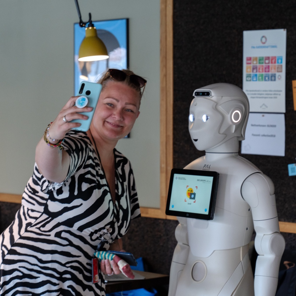 En kvinne tar et bilde av seg selv sammen med Roboten Ari